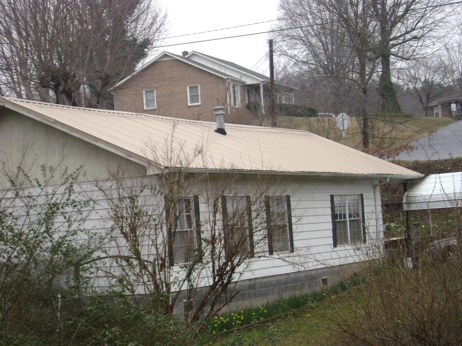 Tan metal roof on a white sided house set into a hillside — Commercial Roofing by Roofing Brothers in Walkersville